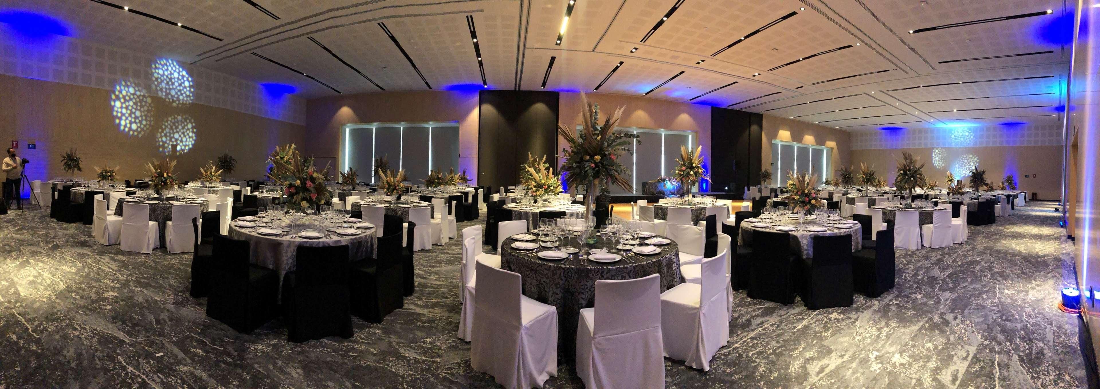 A banquet hall with round tables set for dining, white chairs, and floral centerpieces.