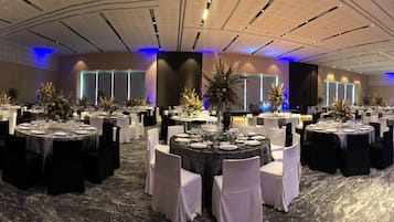 A banquet hall with round tables set for dining, white chairs, and floral centerpieces.