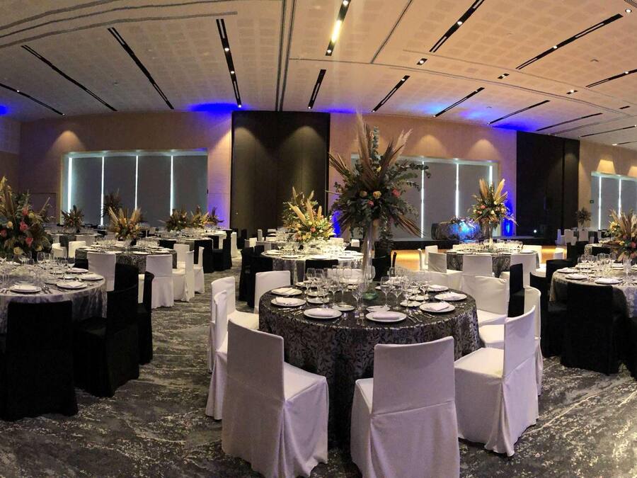 A banquet hall with round tables set for dining, white chairs, and floral centerpieces.