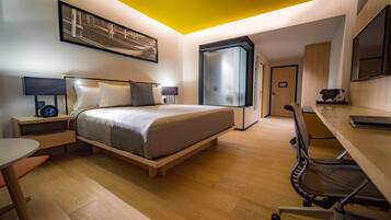 Quarto de hotel moderno com cama, mesas de cabeceira, escrivaninha e uma cadeira.