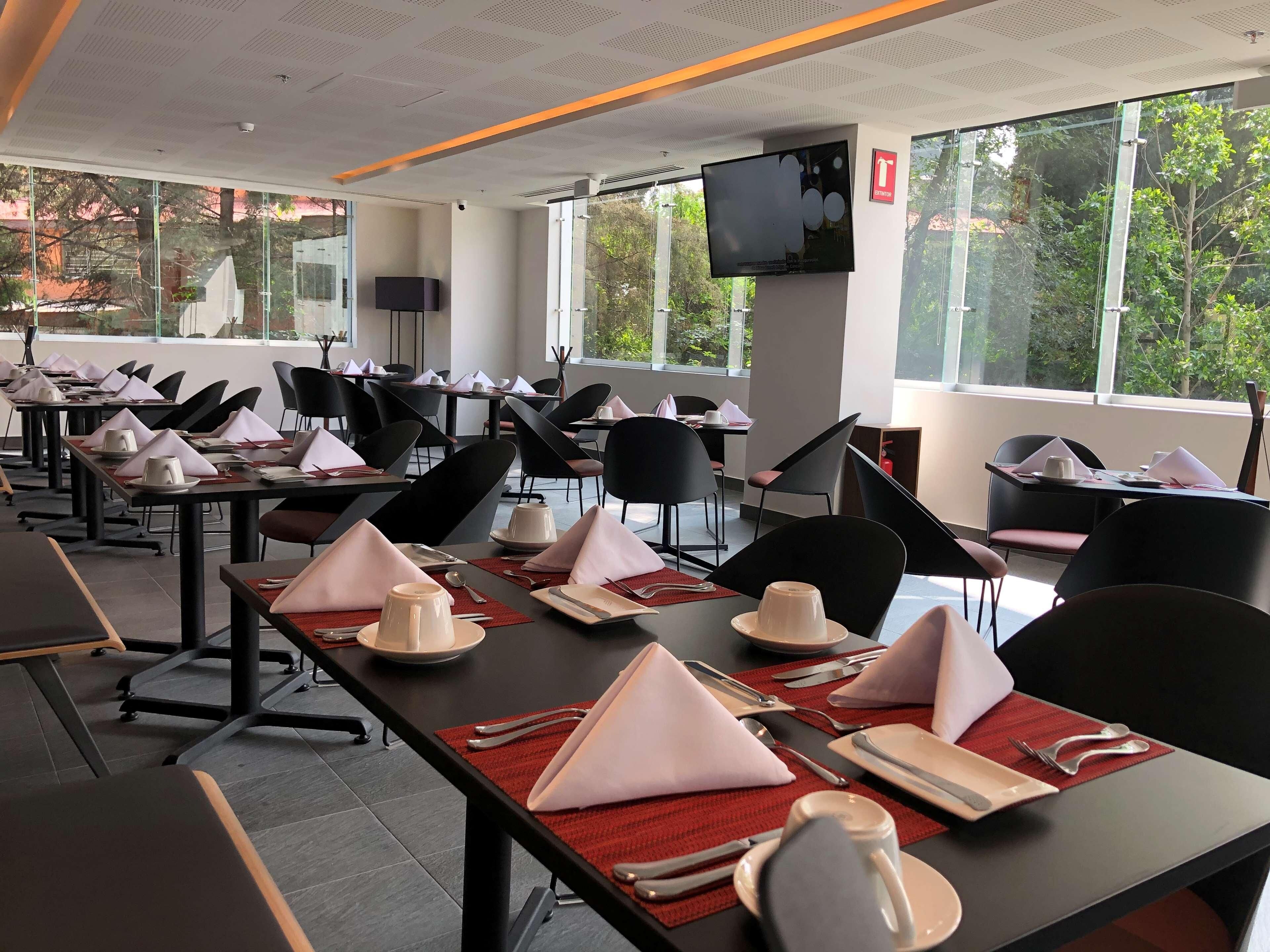 Comedor con mesas dispuestas para varios comensales, con sillas, platos, cubiertos y servilletas.