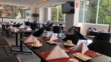 Comedor con mesas dispuestas para varios comensales, con sillas, platos, cubiertos y servilletas.
