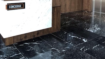 A reception area with a wooden reception desk, a marble floor, and two digital displays on the wall.