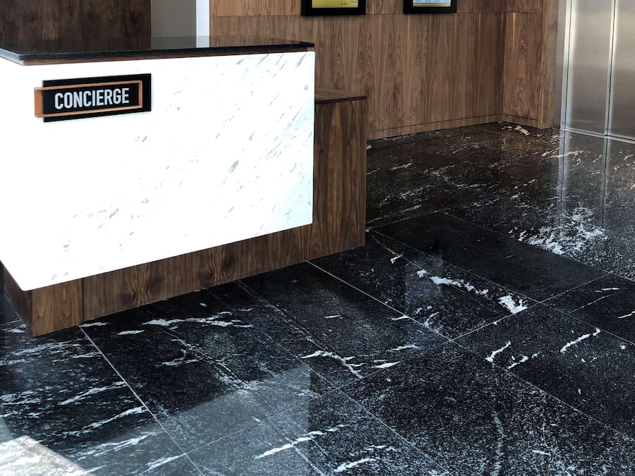 A reception area with a wooden reception desk, a marble floor, and two digital displays on the wall.