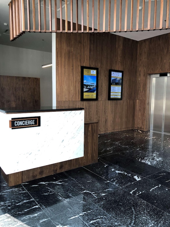 A reception area with a wooden reception desk, a marble floor, and two digital displays on the wall. - Galeria Plaza San Jeronimo (Mexico City)
