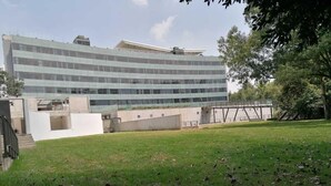 A modern building with a glass facade, a grassy area in front, and a pedestrian bridge in the background. - Galeria Plaza San Jeronimo (Mexico City)