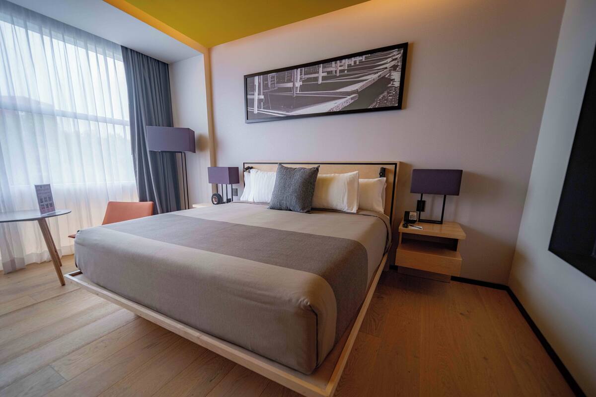 Une chambre d’hôtel moderne avec un grand lit, des tables de chevet, un bureau et une fenêtre avec des rideaux.