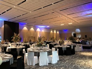 Ein Festsaal mit runden Tischen, weißen Stühlen und floralen Tischdekorationen.