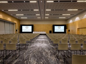 A conference room with rows of chairs, a stage with a screen, and a carpeted floor. - Galeria Plaza San Jeronimo (Mexico City)