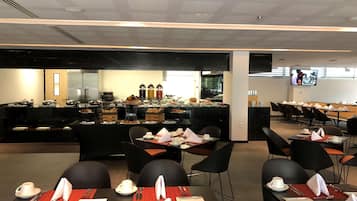 A modern dining area with black chairs and tables, a buffet with various food items, and a television screen on the wall.