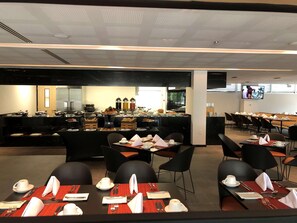 A modern dining area with black chairs and tables, a buffet with various food items, and a television screen on the wall. - Galeria Plaza San Jeronimo (Mexico City)
