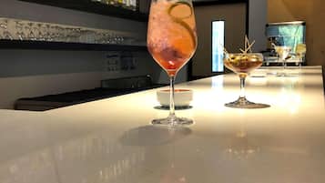 A bar area with a polished countertop, a variety of liquor bottles on shelves, and two glasses of cocktails.