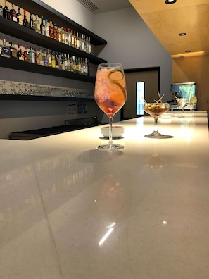 A bar area with a polished countertop, a variety of liquor bottles on shelves, and two glasses of cocktails. - Galeria Plaza San Jeronimo (Mexico City)