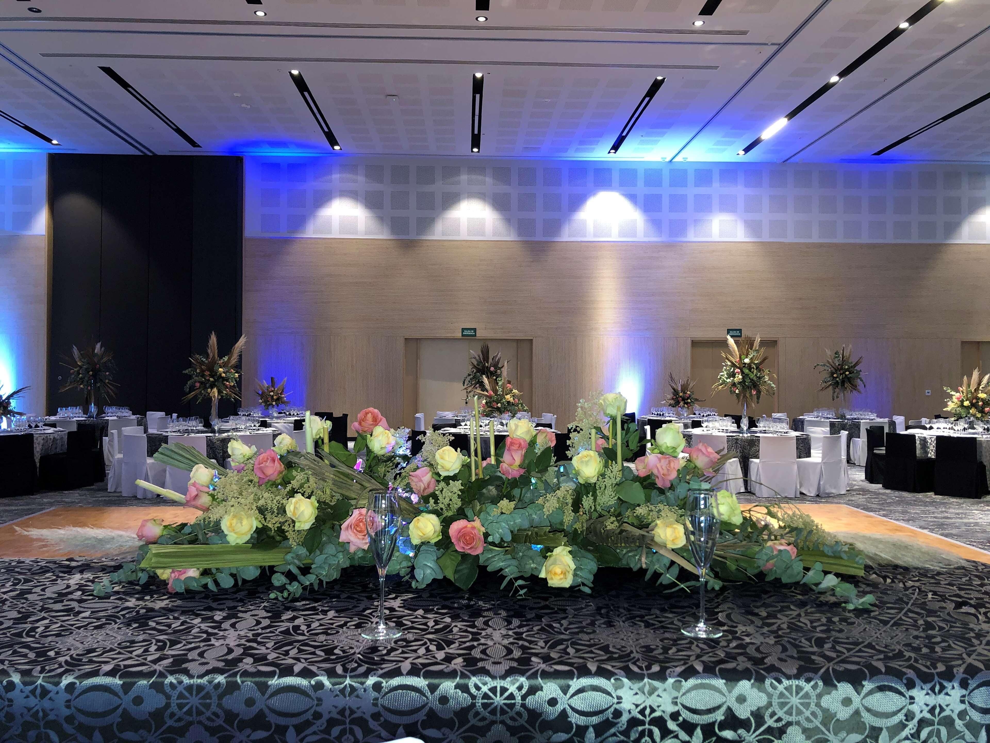 A banquet hall with tables set for a formal event, featuring floral centerpieces and a patterned carpet.