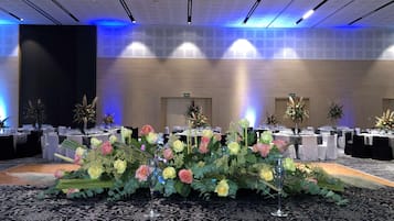 A banquet hall with tables set for a formal event, featuring floral centerpieces and a patterned carpet.