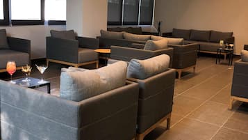 A modern lounge area with multiple sofas and armchairs, a flat-screen TV mounted on the wall, and large windows providing natural light.