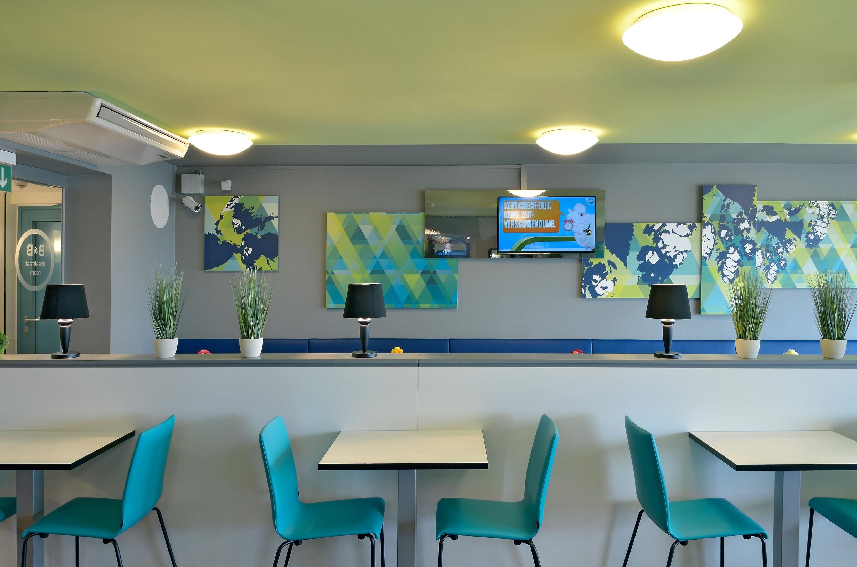 A modern restaurant interior with teal chairs, white tables, and decorative wall art.