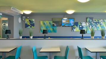 A modern restaurant interior with teal chairs, white tables, and decorative wall art.