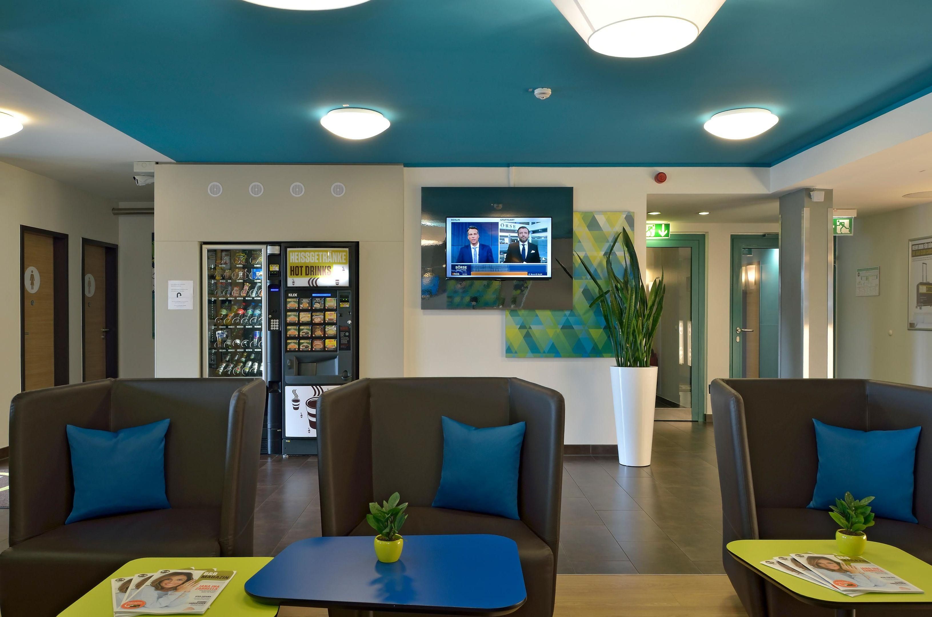 Eine Lobby mit Sitzbereichen, einem Verkaufsautomaten, einem Fernsehbildschirm und einem Blumentopf.