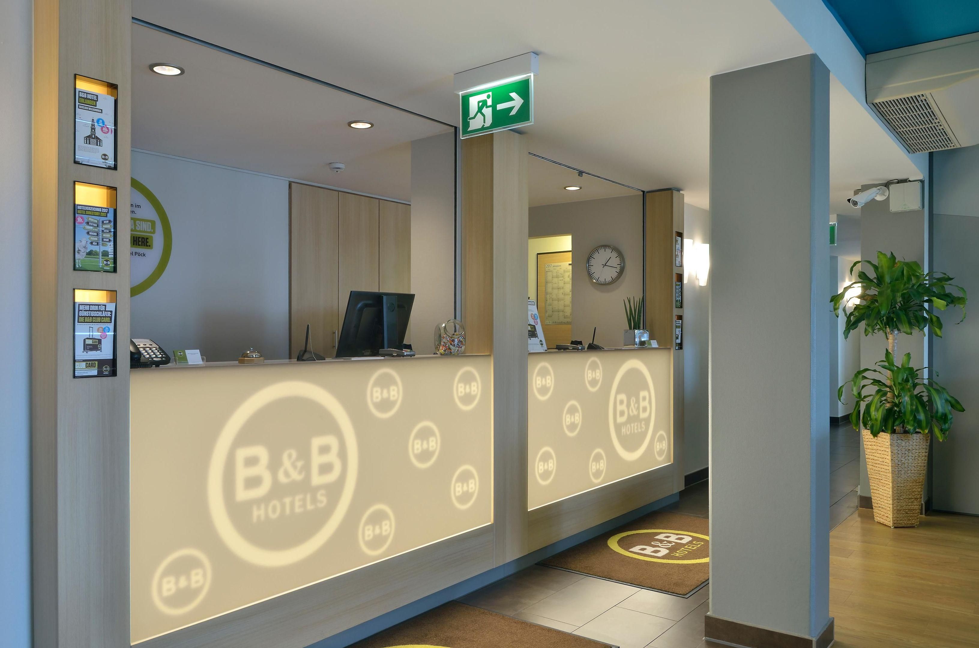 A hotel reception area with a reception desk, a clock, and a green exit sign.