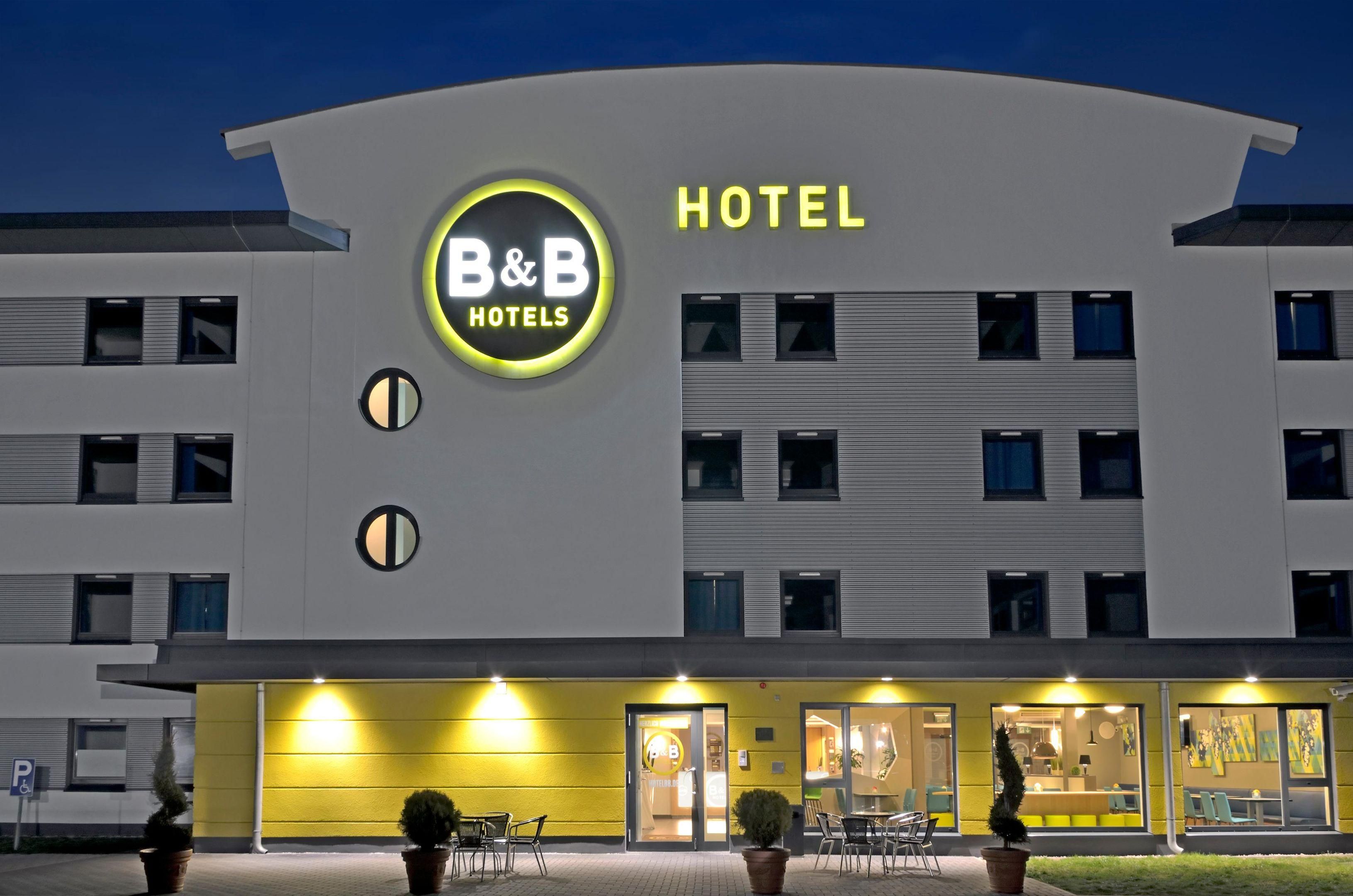 Een modern hotelgebouw met een opvallend B&B Hotels bord, meerdere verdiepingen en een goed verlichte ingang.
