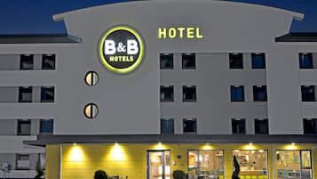 Een modern hotelgebouw met een opvallend B&B Hotels bord, meerdere verdiepingen en een goed verlichte ingang.
