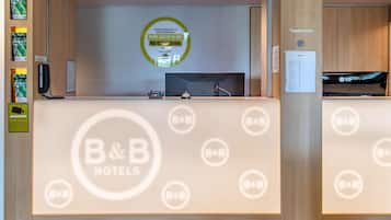A reception desk with a B&B logo, a digital screen, and a sign welcoming guests.