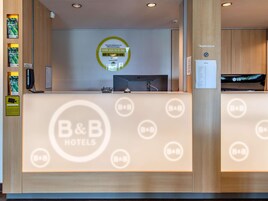 A reception desk with a B&B logo, a digital screen, and a sign welcoming guests.