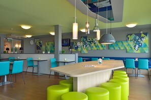 A modern restaurant with bright green and blue chairs, a wooden bar area, and colorful abstract wall art. - B&B Hotel Erlangen (Erlangen)