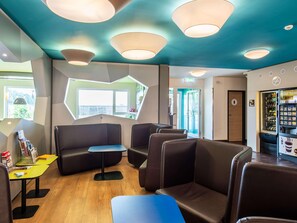 A modern interior with seating areas, a vending machine, and a view through a window. - B&B Hotel Erlangen (Erlangen)