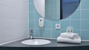 A bathroom with a round mirror, a sink, a towel, and a soap dispenser. - B&B Hotel Erlangen (Erlangen)