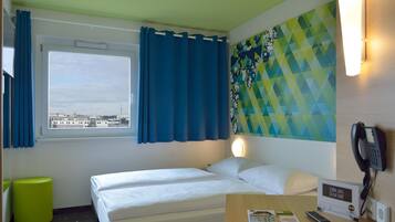 Habitación de hotel con una cama, ventana con cortinas, teléfono en la pared y una revista sobre la mesa.