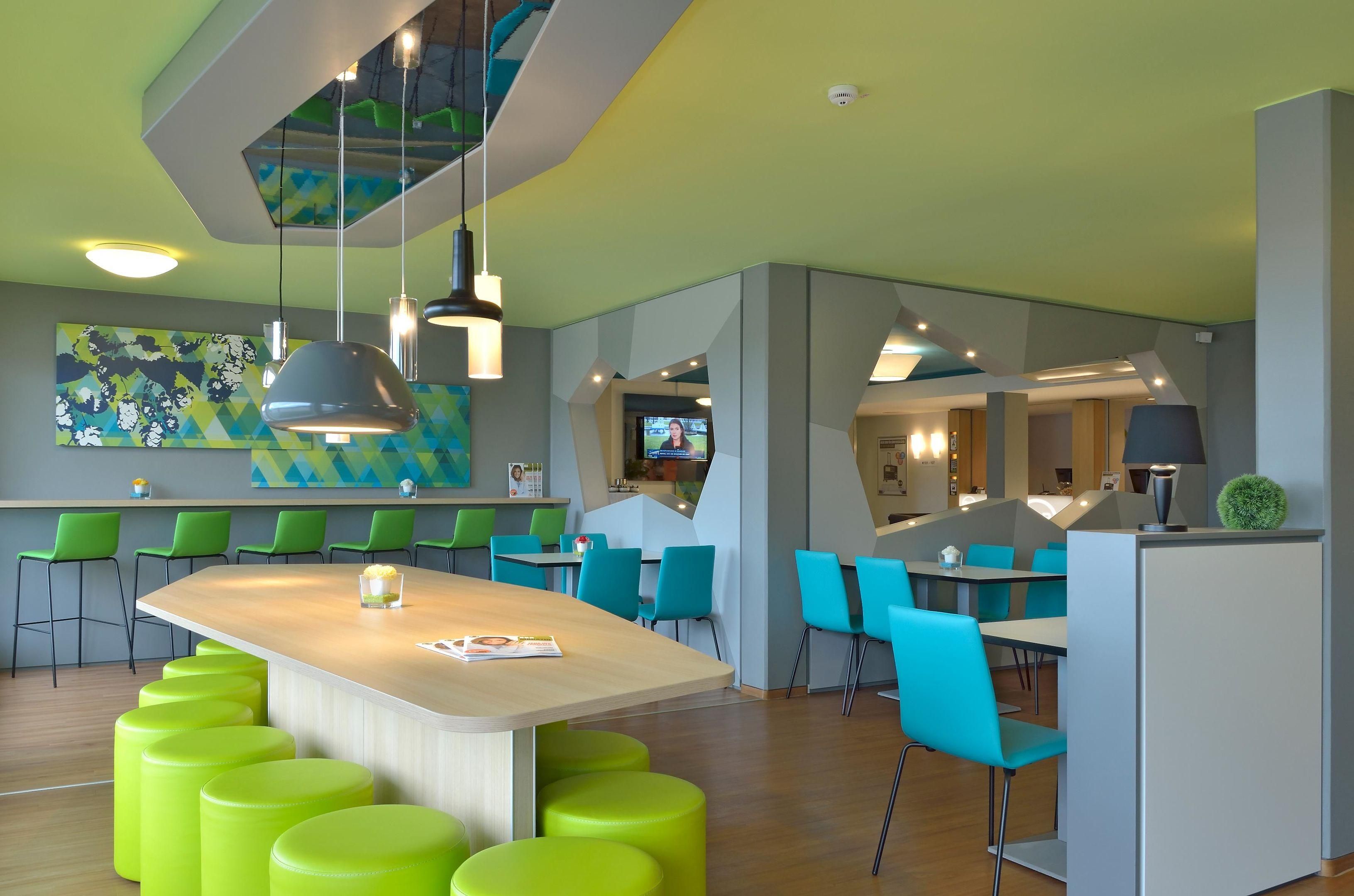 A modern interior with a central island, green chairs, and a large painting on the wall.