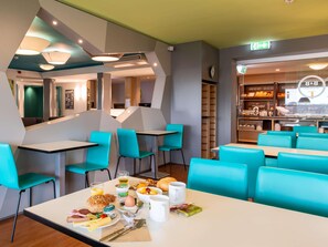 A modern restaurant with teal chairs and tables, a breakfast spread, and a visible exit sign. - B&B Hotel Erlangen (Erlangen)