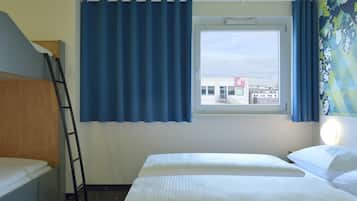 A hotel room with a bed, a window with curtains, a bedside lamp, and a view of a building outside.