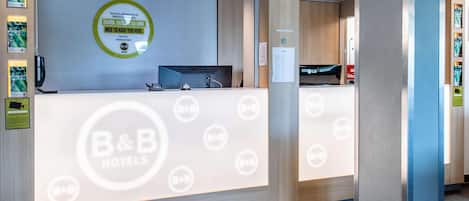 Mostrador de recepción de un hotel B&B con una pantalla digital, un teléfono y un cartel con el nombre del hotel.