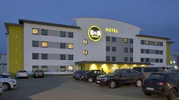 Ein modernes Hotelgebäude mit einem auffälligen B&B Hotels Schild, mehreren Parkplätzen und einer gut beleuchteten Fassade.