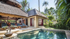 A poolside area with lounge chairs, a thatched-roof structure, and a small building with a red door. - Alam Anda Ocean Front Resort & Spa (Tejakula)
