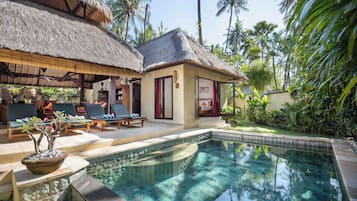 A poolside area with lounge chairs, a thatched-roof structure, and a small building with a red door.