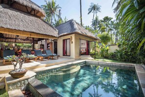 A poolside area with lounge chairs, a thatched-roof structure, and a small building with a red door. - Alam Anda Ocean Front Resort & Spa (Tejakula)