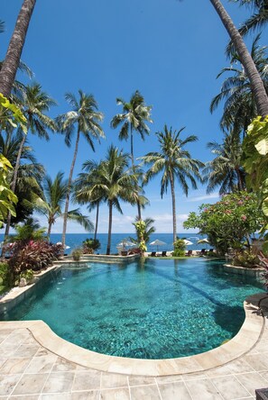 A clear blue pool surrounded by palm trees and a view of the ocean. - Alam Anda Ocean Front Resort & Spa (Tejakula)