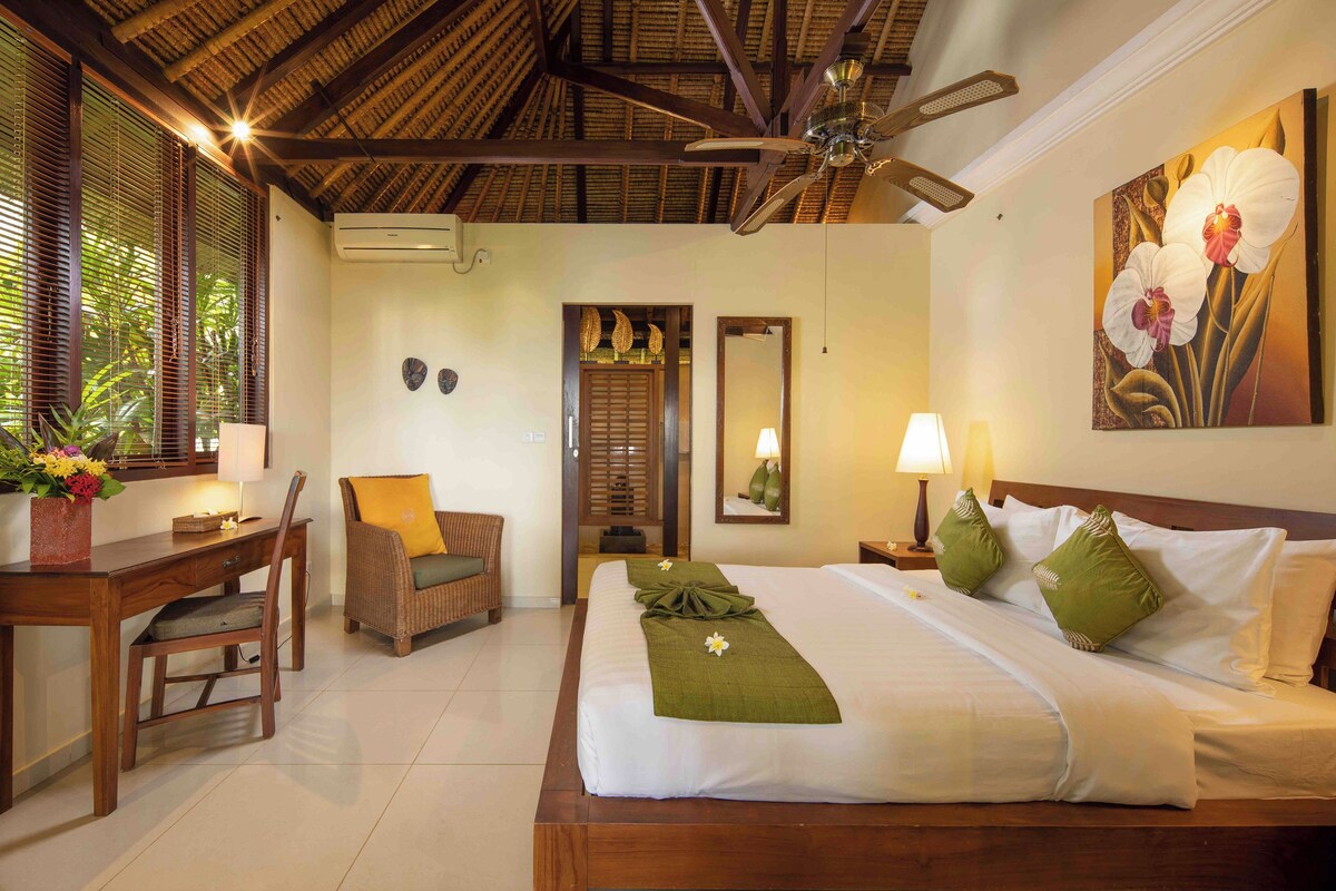 Een goed verlichte hotelkamer met een bed, een bureau, een stoel en een groot raam met jaloezieën.
