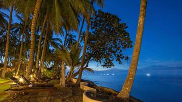 A beachside resort with palm trees, a hammock, and a view of the ocean at dusk.