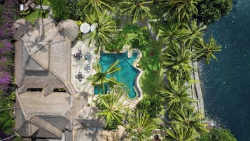 Vista aerea di un resort con piscina, palme e una struttura in pietra.