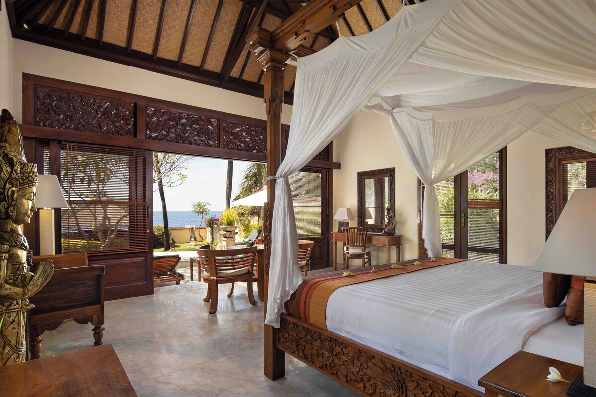 A bedroom with a four-poster bed, wooden furniture, and a view of the sea.