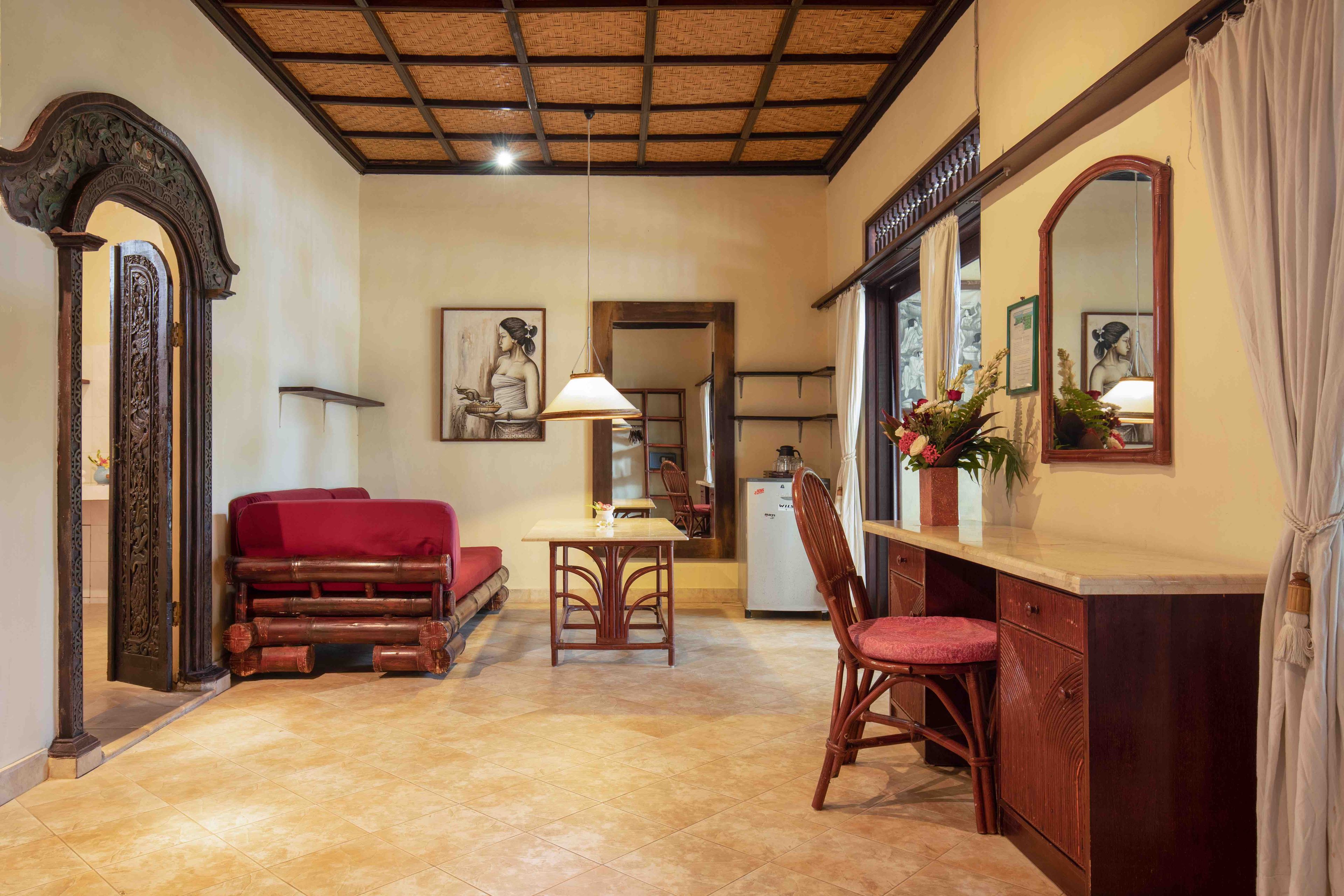 A cozy room with a wooden dining table, a red sofa, and a chair. There is a mirror on the wall and a small refrigerator.
