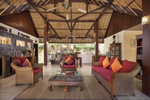 A spacious lounge area with wicker furniture, a glass coffee table, and a ceiling fan. - Alam Anda Ocean Front Resort & Spa (Tejakula)