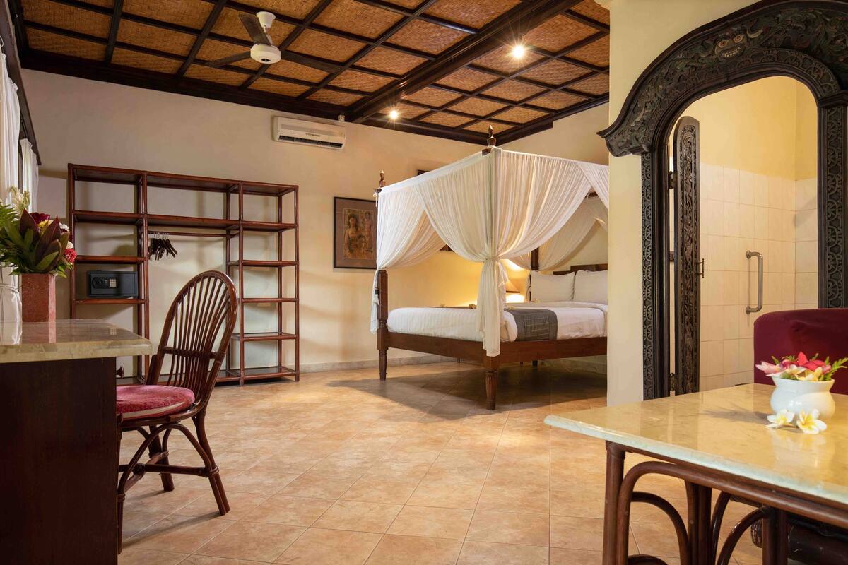 A room with a four-poster bed, a dining table, a chair, a red sofa, and a decorative archway.