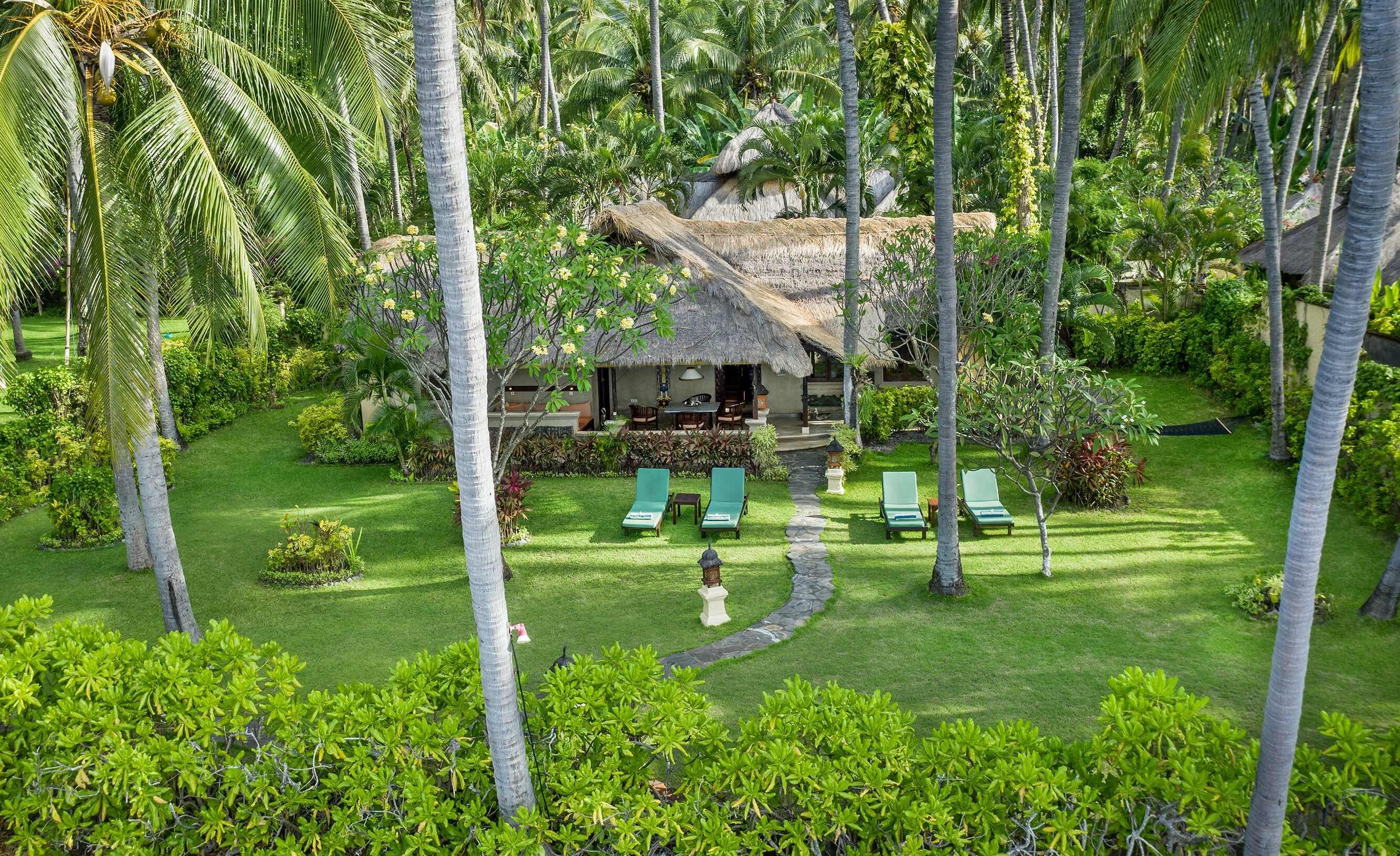 Un resort tropical con una estructura de techo de paja, un césped con sillones de descanso y abundante follaje.