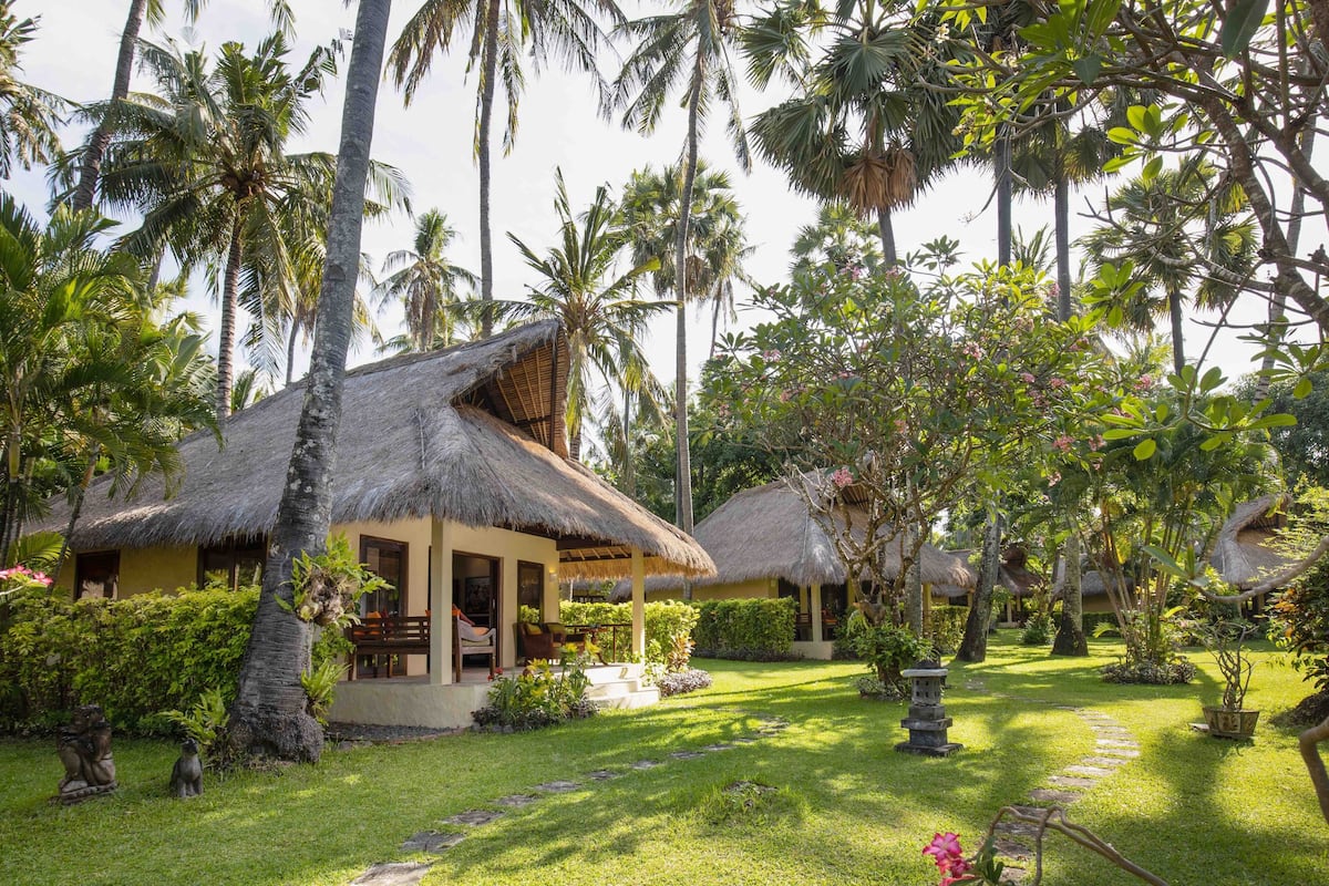 A tropical resort with thatched-roof cottages, lush greenery, and a well-maintained garden.